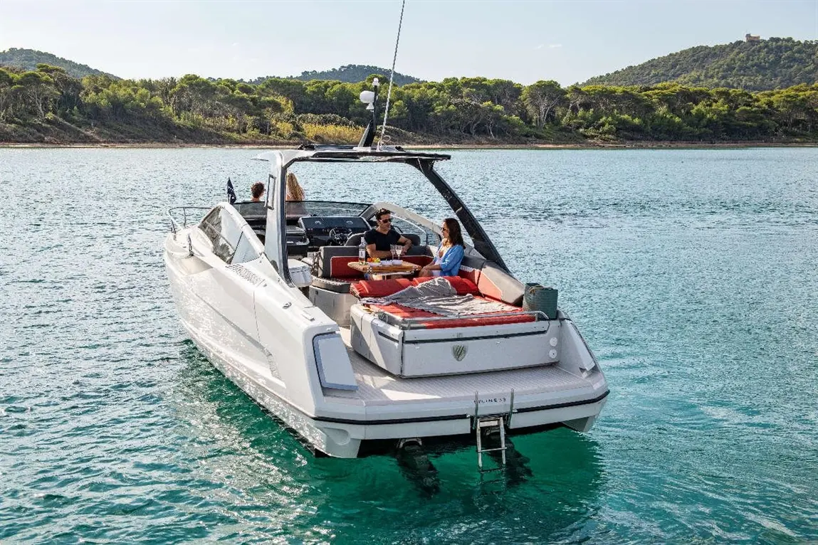 Group enjoying leisure time on a white boat in clear water, with lush green hills in the background and snacks on the table.